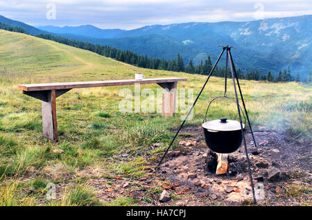 Camping Feuer und Touristen Bowler mit Zubereitung von Speisen in Bergen. Kochen auf dem Feuer unter Feldbedingungen. Lagerfeuer mit Melone Abendessen. Kochen im März Stockfoto