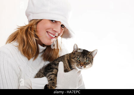 Junge Frau in einem weißen Rollkragenpullover mit Wollmütze hält eine Katze Stockfoto
