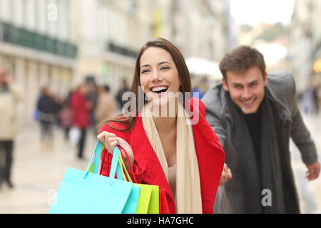 Vorderansicht von ein paar lässige Shopper laufen auf der Straße in Richtung Kamera hielt bunten Einkaufstüten Stockfoto