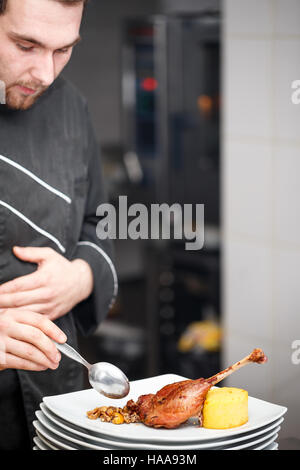 Junge männliche Koch Koch in schwarzer Uniform Dekoration Essen auf dem Teller im Restaurant Großküche Stockfoto