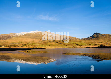 Schneebedeckten Gipfel des Mount Snowdon und Yr Aran spiegeln sich in ruhigen Gewässern Teil eingefroren Llyn y Gader in Snowdonia National Park (Eryri). Rhyd-Ddu Wales UK Stockfoto