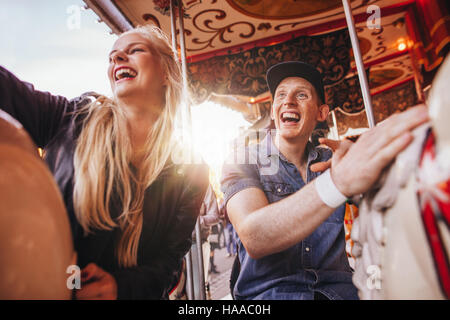 Junger Mann und zwei Frauen auf Karussell am Messegelände. Junges Paar Reiten Pferdekarussell im Vergnügungspark und lachen. Stockfoto