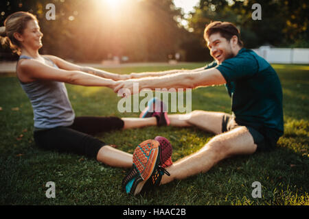 Junge Gesundheit paar stretching-Übung zu tun und wärmen Sie sich im Park. Mann und Frau sitzen zusammen Hand in Hand und trainieren. Stockfoto