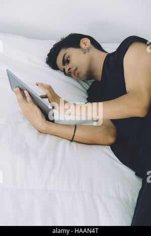 Junge hübsche attraktiven brasilianischen Kerl im schwarzen T-shirt Verlegung im Schlafzimmer auf einem Bett nach morgens schlafen und mit digital-Tablette Stockfoto