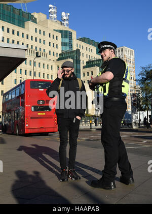 Ein Polizist spricht ein Pendler vor der Secret Intelligence Service, Gebäude, das Hauptquartier des MI6, Vauxhall Busbahnhof in Süd-London, um die Einführung des Anti-Terror-Patrouille Polizeieinheiten quer durch die Hauptstadt zu markieren. Stockfoto