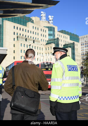 Ein Polizist spricht ein Pendler vor der Secret Intelligence Service, Gebäude, das Hauptquartier des MI6, Vauxhall Busbahnhof in Süd-London, um die Einführung des Anti-Terror-Patrouille Polizeieinheiten quer durch die Hauptstadt zu markieren. Stockfoto