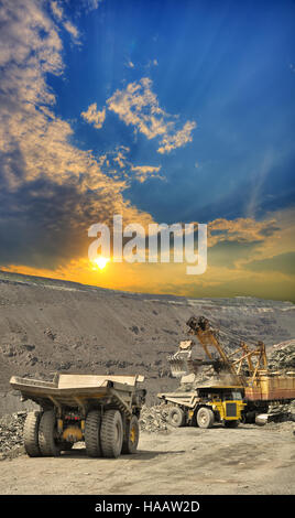 Schwere Muldenkipper werden mit Eisenerz im Tagebau auf Sonnenuntergang im Sommer geladen Stockfoto