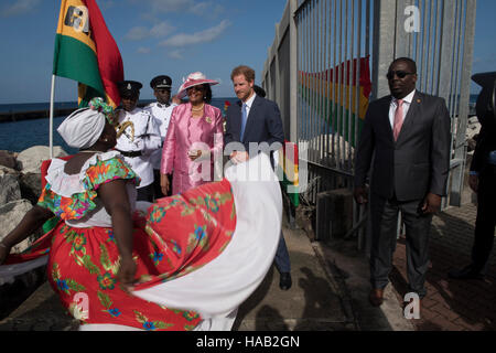 Prinz Harry wird von Gouverneur General Dame Cecile la Grenade (in rosa) begrüßt und Uhren einen Tänzer führen, wie er während der zweiten Etappe seiner karibischen Tour am Kreuzfahrthafen in Grenada, Grenada ankommt. Stockfoto