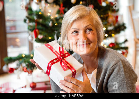 Schöne ältere Frau vor Weihnachtsbaum mit Geschenk Stockfoto