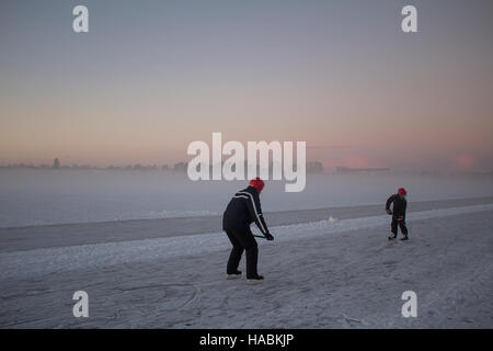 Vater und Sohn Training Eishockey auf einem zugefrorenen See mit einer nebligen Stadt Skyline im Hintergrund. Stockfoto