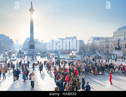 Kundenansturm ein Straßenkünstler in Trafalgar Square in London mit Winter Sonnenuntergang hinter Nelsonsäule ansehen Stockfoto