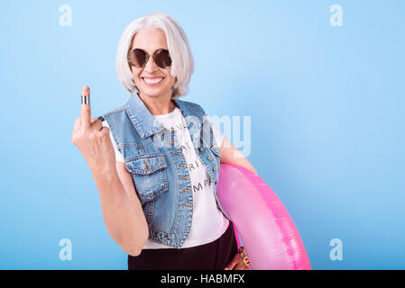 Lächelnde ziemlich senior Frau zeigt ihr Mittelfinger. Stockfoto