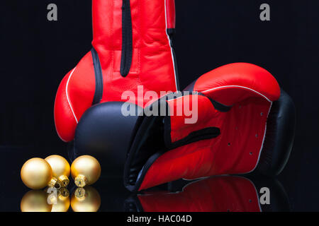 Rote und schwarze Boxhandschuhe und Weihnachtsdekoration auf schwarzem Glastisch. Weihnachten ist kein Kampf um die Weihnachtsgeschenke. Stockfoto