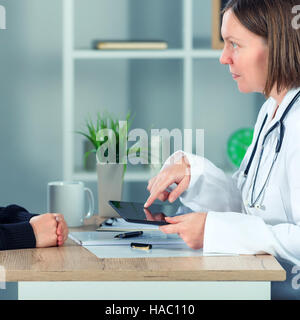 Ärztin, die Patienten mit Hilfe digitaler Tablet-Computer im Krankenhaus Büro ärztliche Untersuchung Ergebnisse vorlegen Stockfoto