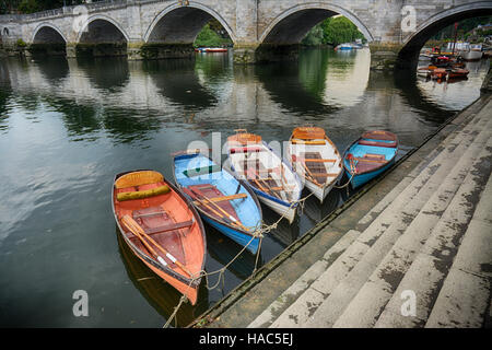 Traditionellen Ruderboote zu mieten, festgemacht an die Bank von Fluß Themse in London Richmond mit Richmond Bridge im Hintergrund Stockfoto