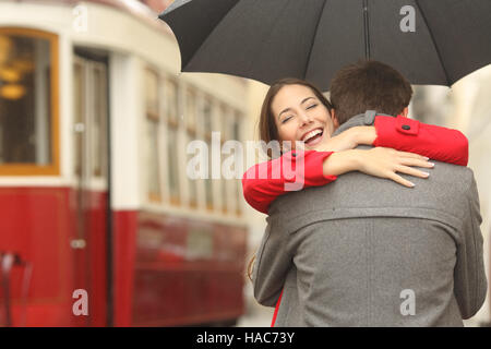 Nach einer Reise von ein glückliches Paar umarmt auf der Straße in einer Tram-Station an einem regnerischen Tag unter einem Regenschirm begegnen Stockfoto