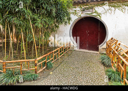 Traditionelle chinesische Gartenanlage - shut weiße Umfassungsmauer mit Schlüsselloch Holztür von kleinen Bambus-Pflanzen und gehen weg mit Cobbleston verziert Stockfoto