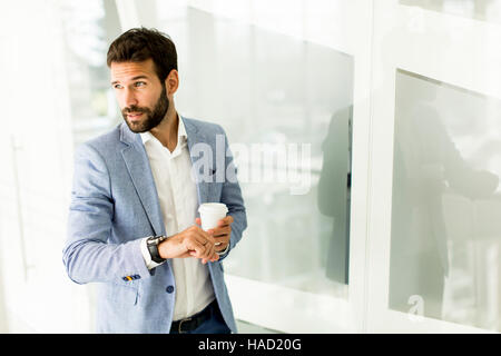 Geschäftsmann im Anzug, eine Tasse Kaffee in einem Bürogebäude und Blick auf die Uhr Stockfoto