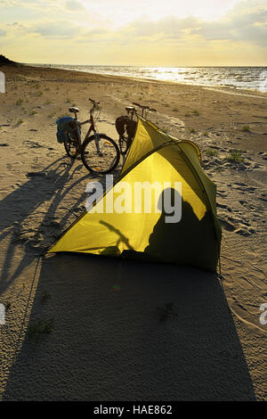 Fahrräder und Shelter Zelt am leeren Strand am Baltischen Meer, Hintergrundbeleuchtung bei Sonnenuntergang. Stegna, Pommern, Nordpolen. Stockfoto