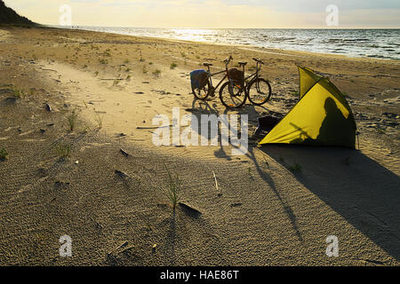 Fahrräder und Shelter Zelt am leeren Strand am Baltischen Meer, Hintergrundbeleuchtung bei Sonnenuntergang. Stegna, Pommern, Nordpolen. Stockfoto