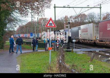 OLDENZAAL, Niederlande - 27. November 2016: Unbekannte Menschen warten auf einen vorbeifahrenden Behälter trainieren auf einer gesicherten Zug-Kreuzung Stockfoto