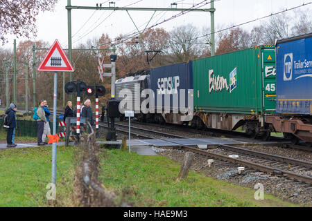 OLDENZAAL, Niederlande - 27. November 2016: Unbekannte Menschen warten auf einen vorbeifahrenden Behälter trainieren auf einer gesicherten Zug-Kreuzung Stockfoto