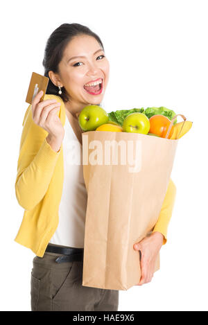 Glückliche junge Asiatin Shopper, Hände halten Einkaufstaschen voller Lebensmittel und Kreditkarte, zeigt isoliert auf weißem Hintergrund stehen. Stockfoto