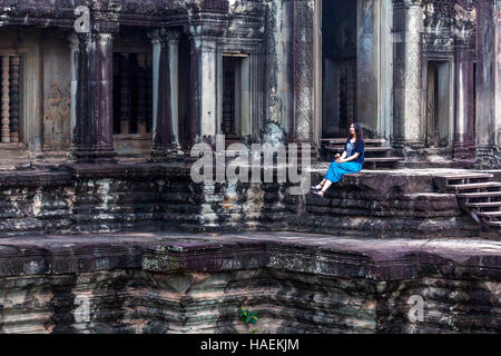 Ein Tourist sitzt unter den massiven Steinen-Strukturen an der alten Tempelanlage Angkor Wat in Siem Reap, Kambodscha. Stockfoto