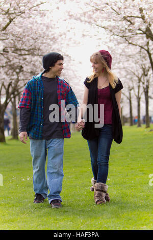 Junger Mann und Frau zu Fuß durch einen Park mit Blick auf einander und Hand in Hand. Stockfoto