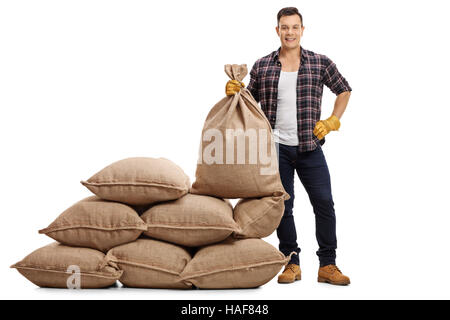 Voller Länge Porträt eines jungen Landwirts stehen neben einem Stapel von Säcken und halten einem Leinensack isoliert auf weißem Hintergrund Stockfoto