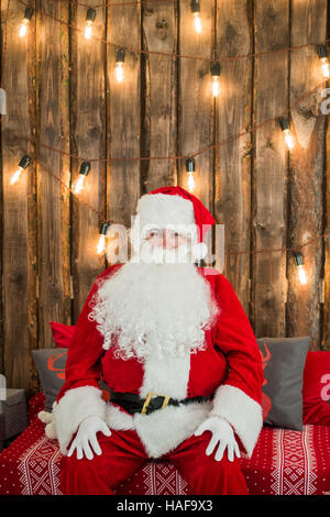 Traditionellen Weihnachtsmann auf der Couch sitzen und erholend. Weihnachten. Roten Hintergrund. Stockfoto