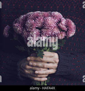 Nahaufnahme von Händen eines Mannes in dunklen Pullover hält ein Bouquet von roten Wildblumen Stockfoto