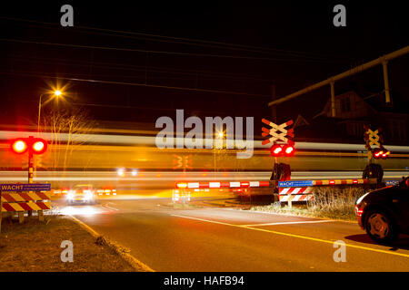 Schranke am Bahnübergang mit einem vorbeifahrenden Zug und wartenden Autos geschlossen Stockfoto