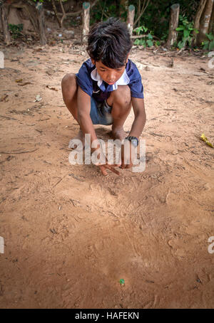 Dorfjunge junge kambodschanischen in der Nähe von Banteay Srei, Kambodscha spielt Murmeln im Dreck. Stockfoto