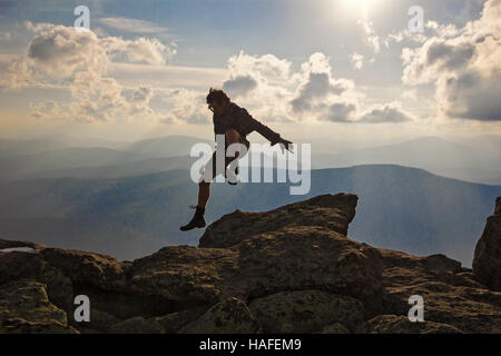 Wanderer mit Rucksack springen über Felsen Sonnenuntergang Himmel im Hintergrund Stockfoto