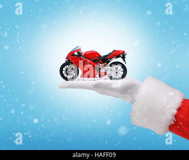 Hand in Santa Claus Kostüm hält rot Motorrad. Studioaufnahme des Mannes Hand hält vorhanden. Frohe Weihnachten & Silvester-Konzept. Closeup auf Stockfoto
