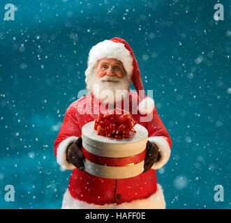 Santa Claus in Schneefall mit Geschenken für Kinder. Frohe Weihnachten & Silvester-Konzept. Hautnah auf blauen Hintergrund jedoch unscharf. Kopieren Sie Raum. Stockfoto