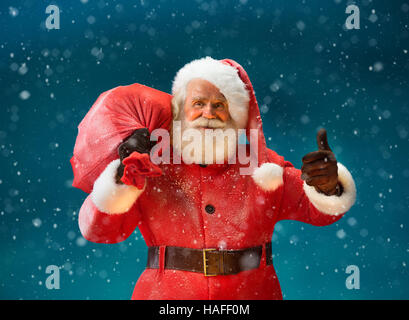 Happy Santa Claus gestikulieren Daumen mit big-Bag voller Geschenke an die Kinder. Frohe Weihnachten & Silvester-Konzept. Stockfoto