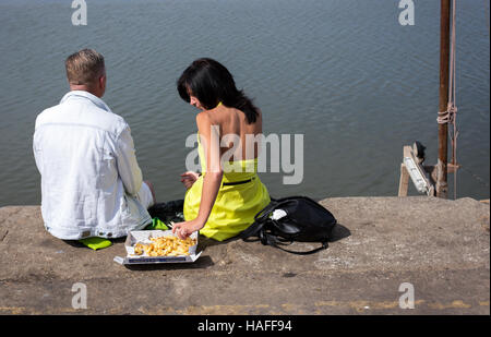 Mann und Frau Essen Fish &amp; Chips unter freiem Himmel sitzen am Kai am Meer Stockfoto