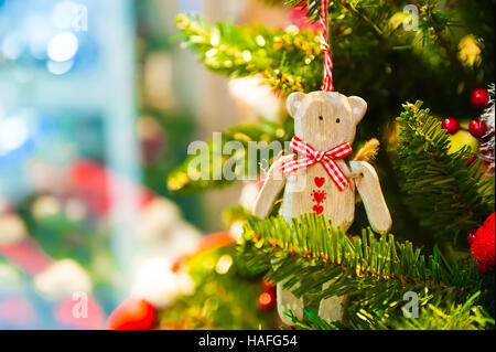 Altes Holzspielzeug Bär mit einer roten Schleife Schleife hängen Weihnachtsbaum im Hintergrund andere Dekorationen und Girlanden. Textfreiraum. Stockfoto