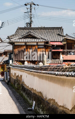 Japan, Tatsuno. Verwittert - weißen Putz überdachte Wand Holz- alten ländlichen Japanischen Haus mit kleinen, dreieckigen Fenster in der zurück führt. Stockfoto