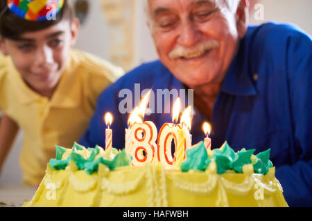 Enkel und Familie senior woman 80 Geburtstag feiern. Großvater bläst Kerzen mit Nummer 80 auf Kuchen und lächelnd. Stockfoto