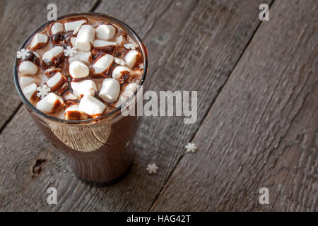 Winter heißer Kakao mit Marshmallows, Schokoladen-Sirup, Zucker Schneeflocken in ein hohes Glas auf einem hölzernen Hintergrund. Stockfoto