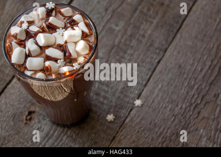 Winter heißer Kakao mit Marshmallows, Schokoladen-Sirup, Zucker Schneeflocken in ein hohes Glas auf einem hölzernen Hintergrund. Stockfoto