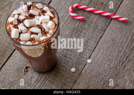 Winter heißer Kakao mit Marshmallows, Schokoladen-Sirup, Zucker Schneeflocken in ein hohes Glas auf einem hölzernen Hintergrund. Stockfoto