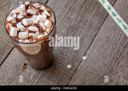 Winter heißer Kakao mit Marshmallows, Schokoladen-Sirup, Zucker Schneeflocken in ein hohes Glas auf einem hölzernen Hintergrund. Stockfoto