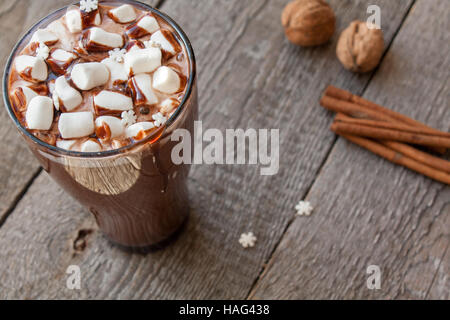 Winter heißer Kakao mit Marshmallows, Schokoladen-Sirup, Zucker Schneeflocken in ein hohes Glas auf einem hölzernen Hintergrund. Stockfoto