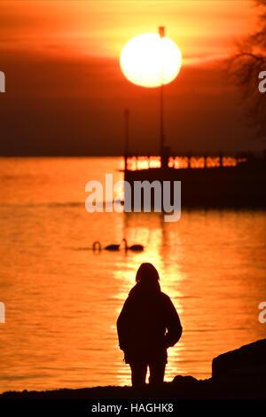 Friedrichshafen, Deutschland. 1. Dezember 2016. Eine Frau wacht die untergehende Sonne über dem Bodensee in Friedrichshafen, Deutschland, 1. Dezember 2016. Foto: Felix Kästle/Dpa/Alamy Live News Stockfoto