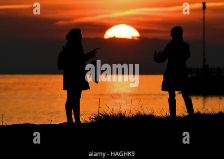 Friedrichshafen, Deutschland. 1. Dezember 2016. Zwei Frauen beobachten den Sonnenuntergang über dem Bodensee in Friedrichshafen, Deutschland, 1. Dezember 2016. Foto: Felix Kästle/Dpa/Alamy Live News Stockfoto