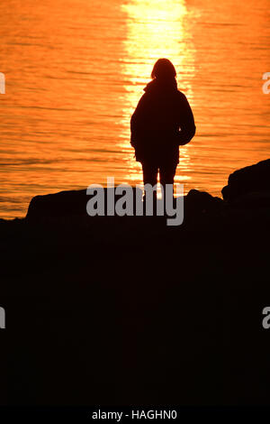 Friedrichshafen, Deutschland. 1. Dezember 2016. Eine Frau wacht die untergehende Sonne über dem Bodensee in Friedrichshafen, Deutschland, 1. Dezember 2016. Foto: Felix Kästle/Dpa/Alamy Live News Stockfoto